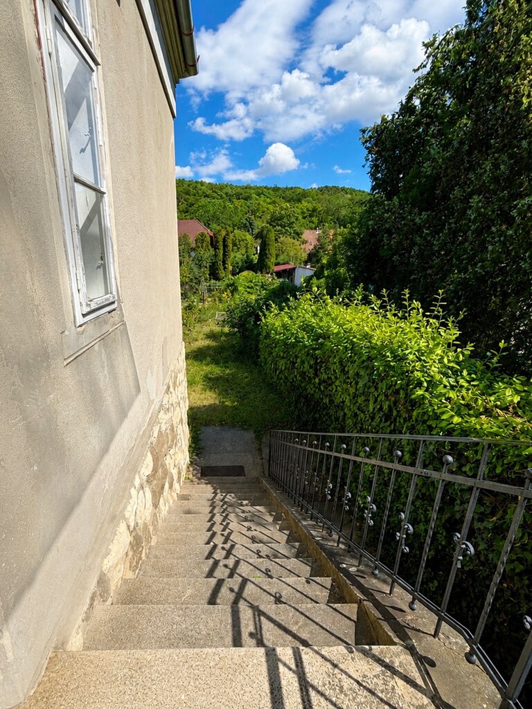 Külső kő lépcső fém korláttal a villa mellett, zöldellő domboldallal a háttérben
